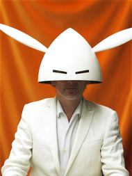 Portraitfoto von Jan Lauwers vor orangenem HIntergrund mit einer weißen Maske