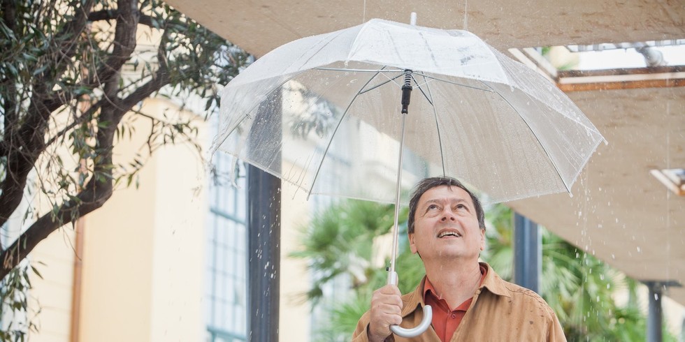 Der Künstler Paul DeMarinis steht mit einem durchsichtigen Regenschirm unter seiner Installation und schaut nach oben